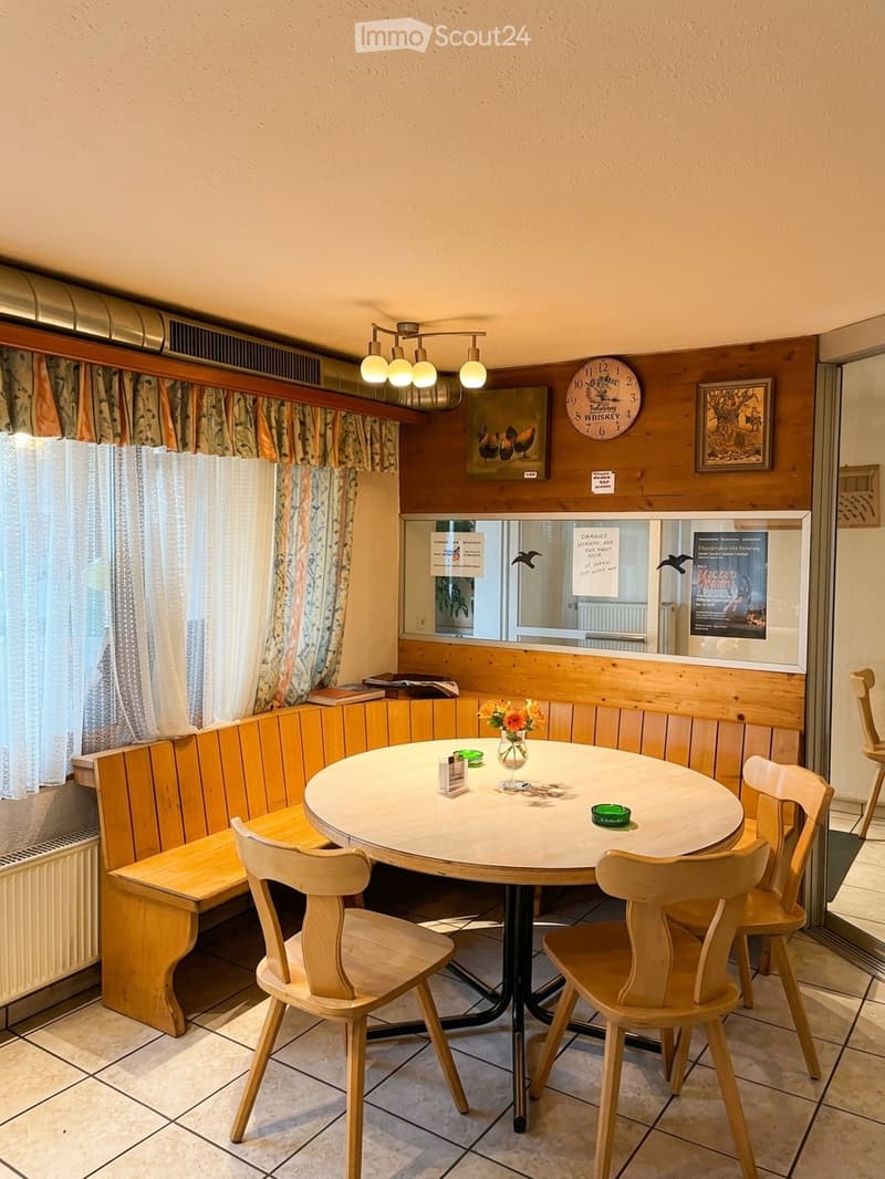 Cozy dining area with a round table surrounded by wooden chairs and a bench, a vase with flowers, and a clock on the wall.