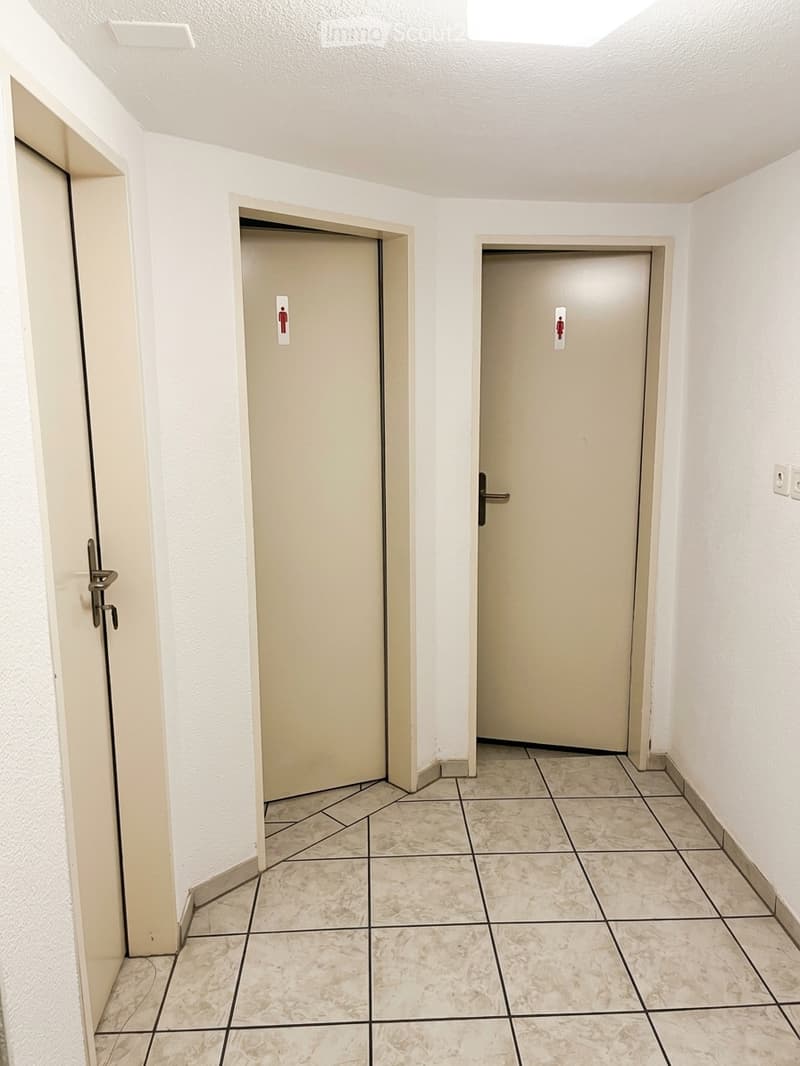 Empty hallway with tiled floor, white walls, and two closed doors with gender symbols.