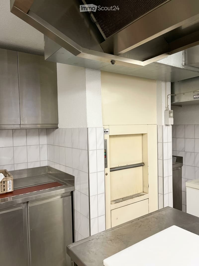 Commercial kitchen with stainless steel cabinets, countertop, oven, and range hood.