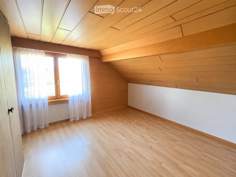 Empty room with wooden flooring, white walls, and a large window with sheer curtains. The ceiling has exposed wooden beams, and there is a built-in white cabinet on one wall.