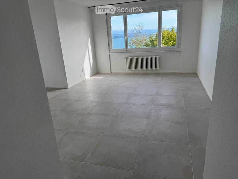 Empty room with tiled floor, large window offering a scenic view, radiator, and white walls.