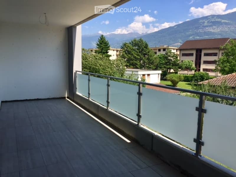 Balcony with a modern glass railing, tiled floor, and scenic mountain view in the background.