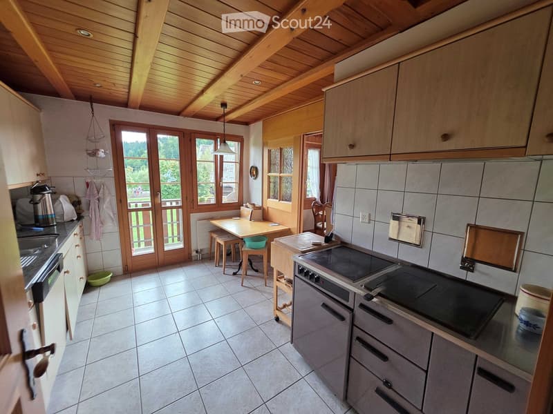 Bright kitchen with wooden beams, large windows, and a dining area. Features a modern electric stove, sink, and ample cabinetry.