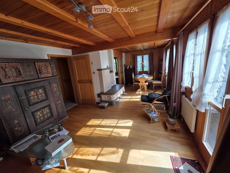 Bright living room with wooden beams, large windows, a glass coffee table, a sofa, a fireplace, and a dining area with a table and chairs.