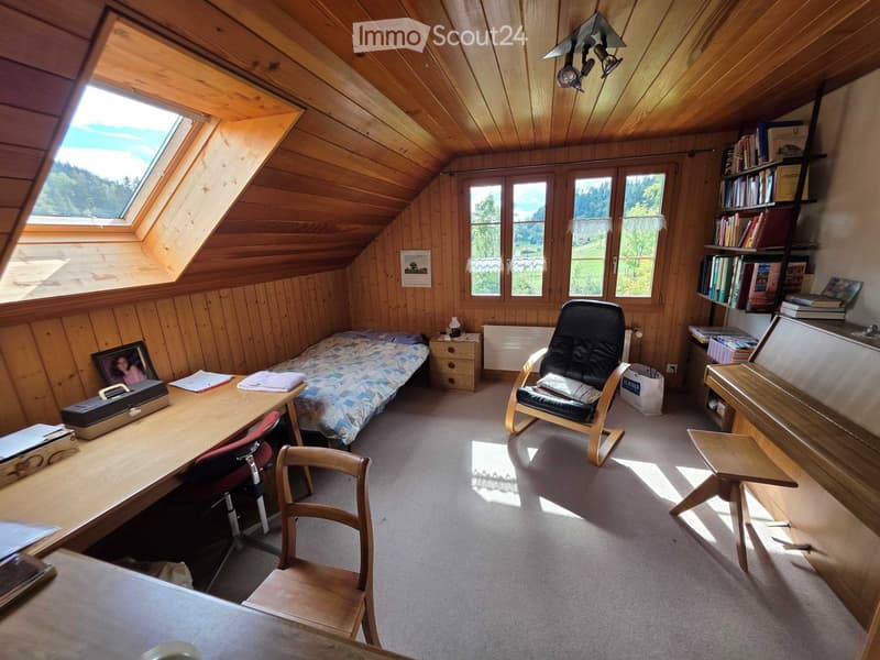 Cozy attic bedroom with wooden walls and ceiling, featuring a small bed, desk, chair, bookshelf, and a window with scenic view.