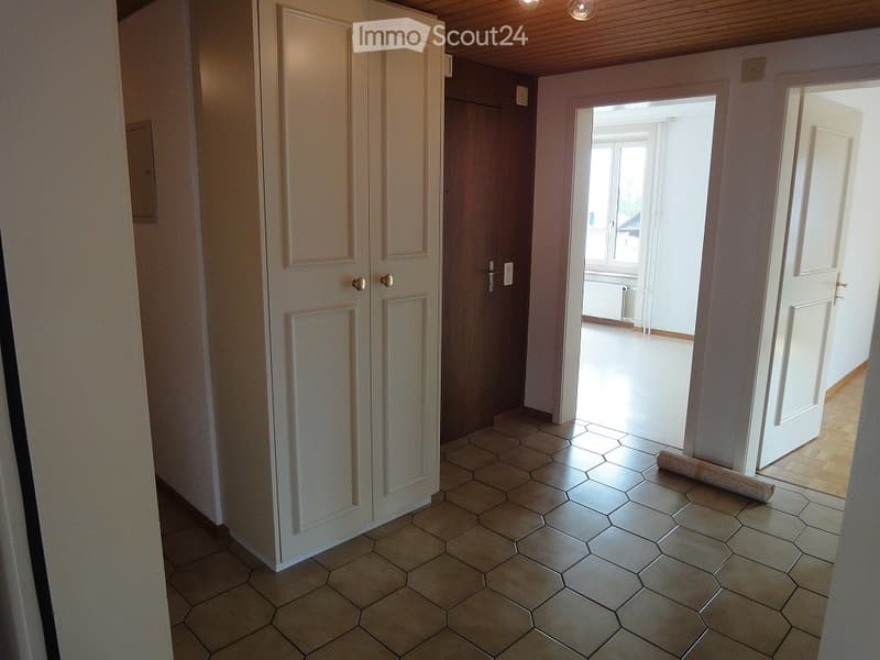 Empty hallway with hexagonal tiled floor, white walls, and a wooden door leading to another room.