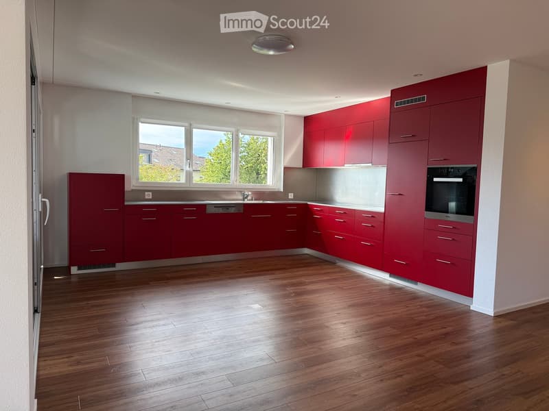 Modern kitchen with red cabinets, wooden flooring, and stainless steel appliances including an oven and sink.