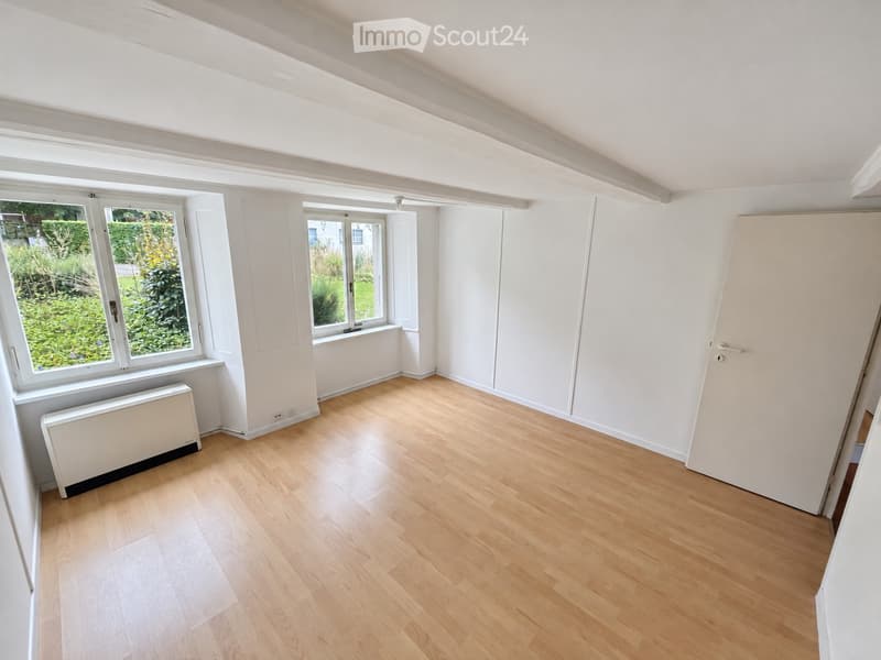 Empty room with wooden flooring, white walls, large windows, and a radiator. No furniture or equipment present.