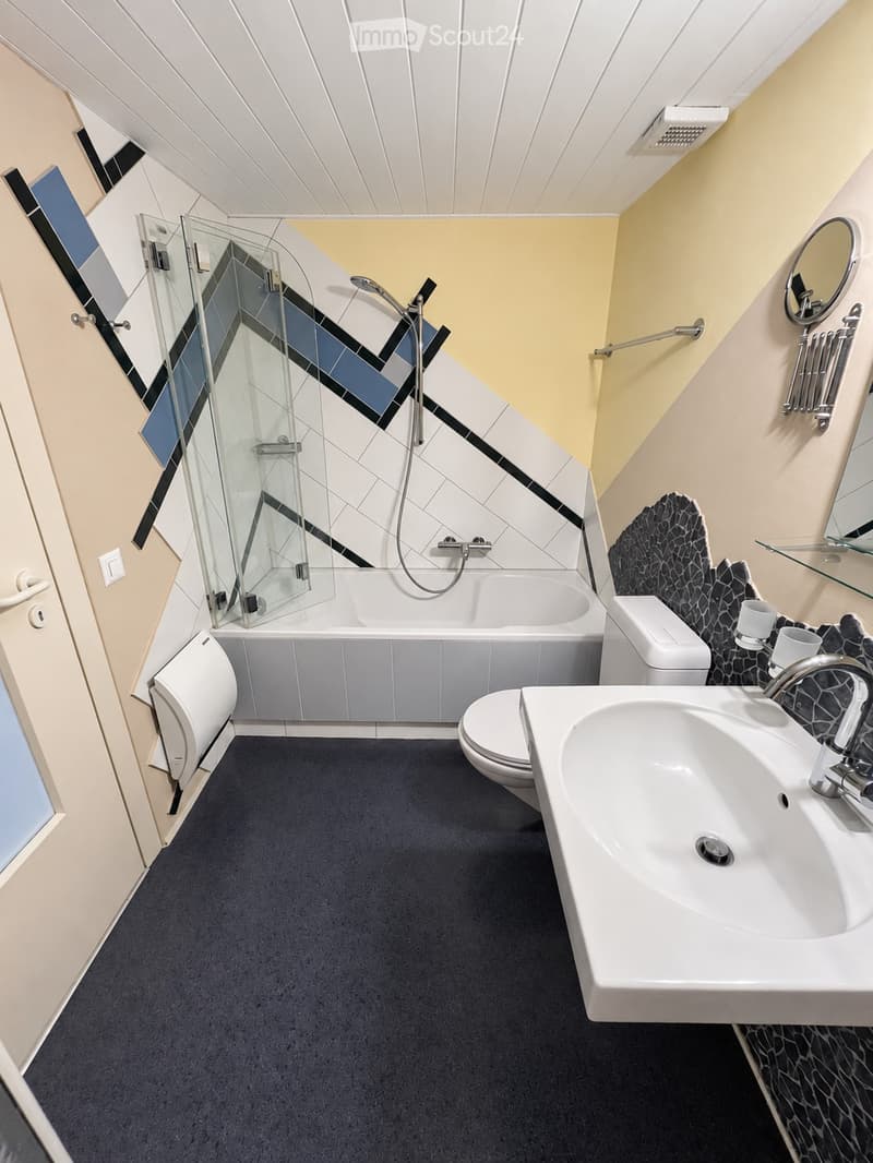 Modern bathroom with a bathtub, toilet, sink, and shower area. Features a geometric tile design on the walls and a sleek, contemporary aesthetic.