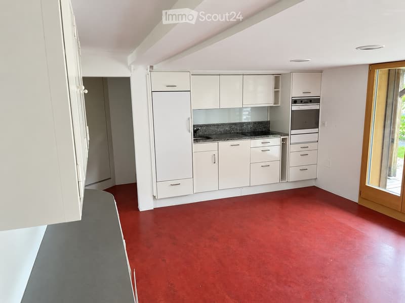Modern kitchen with white cabinets, a dark countertop, and a red floor. Features a sink, oven, and a sliding glass door leading outside.