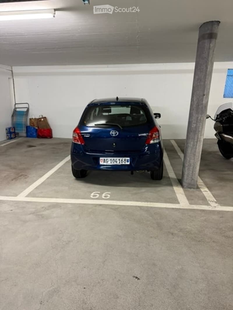 Underground parking space with a blue car parked in bay number 66, along with a scooter and some bags on the left side.