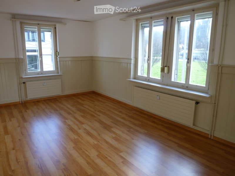 Empty room with wooden flooring, white walls, and large windows with radiators beneath them.