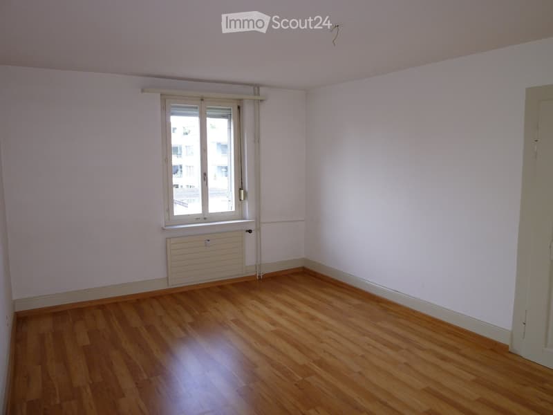 Empty room with wooden flooring, white walls, a window with blinds, and a radiator below the window.