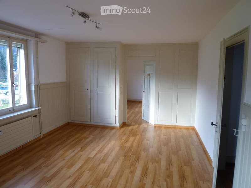 Empty room with wooden flooring, white walls, multiple doors, and a window with a radiator below it.
