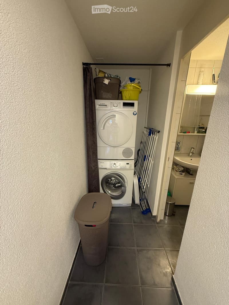A compact bathroom with a washing machine, sink, mirror, cabinet, and laundry rack.