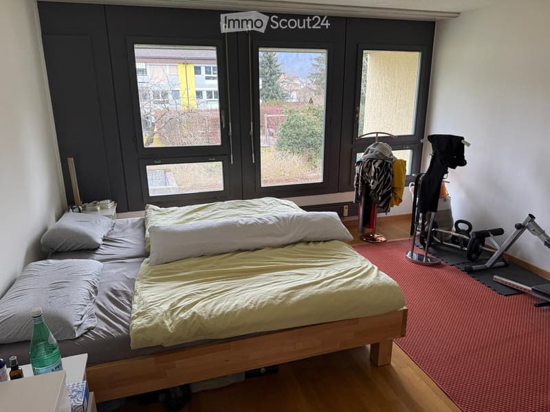 A small bedroom with a wooden bed, pillows, a clothing rack, and an exercise bike in the corner.