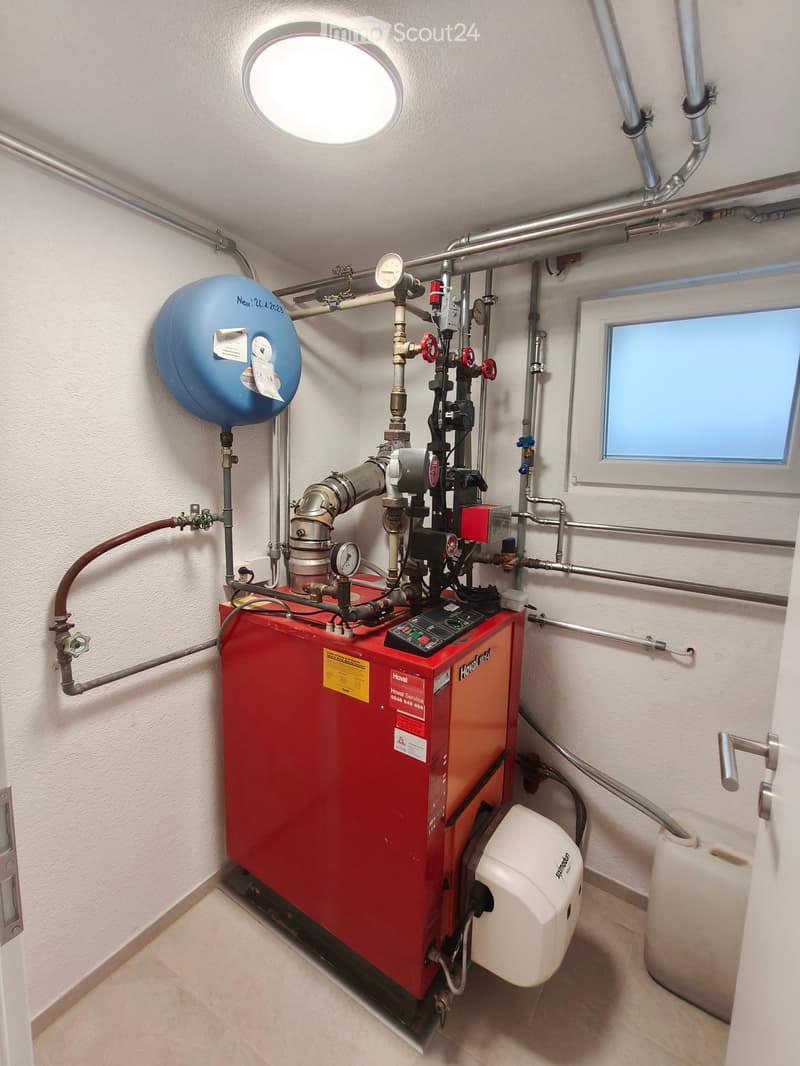 A modern bathroom utility area with a red water heater, pressure vessel, control panel, and various pipes and valves.