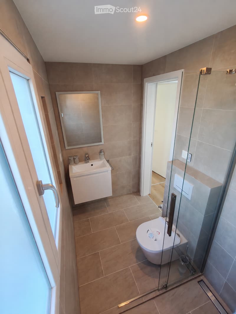 Modern bathroom with beige tiles, a white sink with a mirror, a toilet, and a glass-enclosed shower area.
