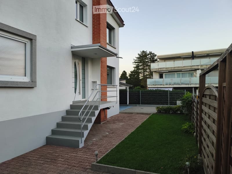 Garden area with a well-maintained lawn, brick pathway, steps leading to a house entrance, and a wooden fence.