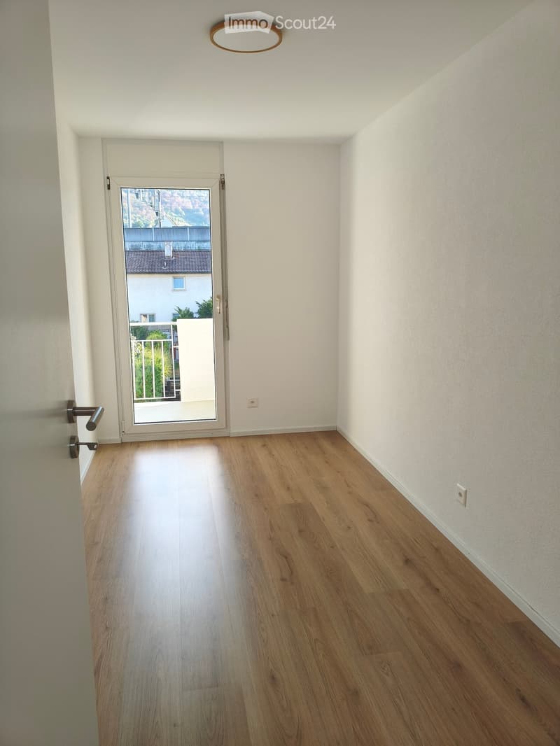 Empty hallway with wooden flooring, white walls, and a sliding glass door leading outside.