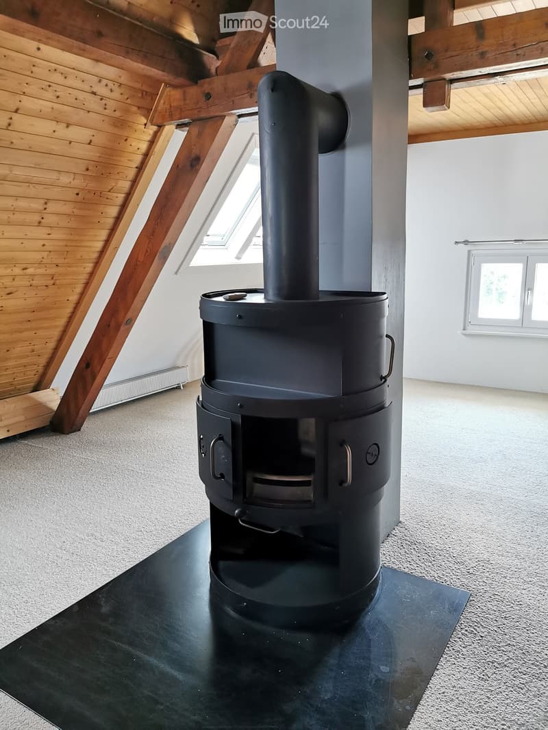 Modern room with exposed wooden beams, a sleek black wood-burning stove, and large windows allowing natural light.