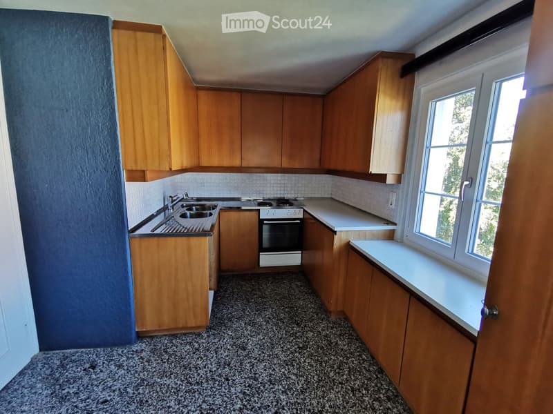 Empty kitchen with wooden cabinets, a sink, and an oven, featuring a tiled backsplash and a window letting in natural light.