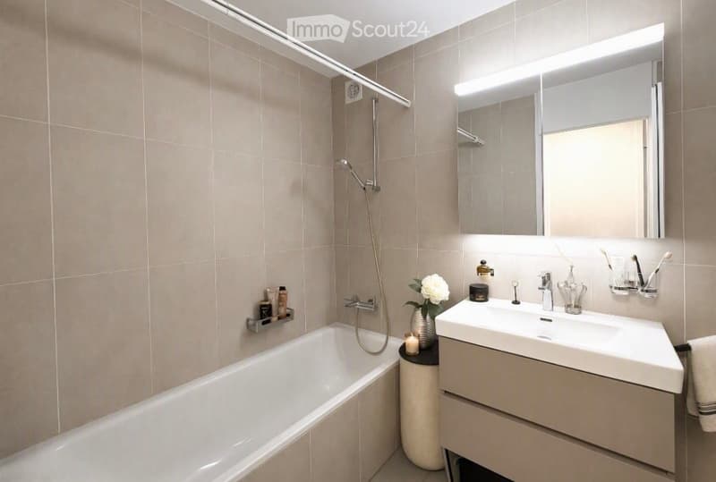 Modern bathroom with a bathtub, sink, large mirror, and shower. Includes a flower vase, candle, and toothbrush holder.