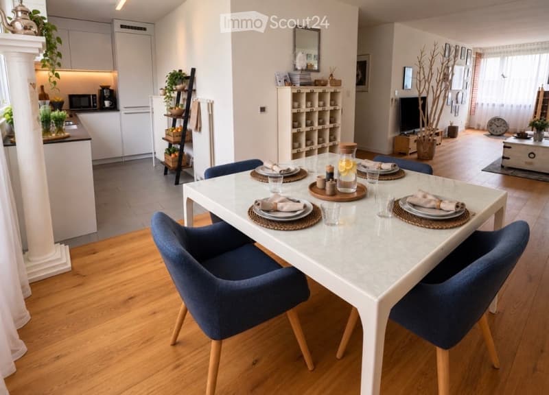 Open-plan living and dining area with a white dining table, blue chairs, modern kitchen, shelves, and decorative items.