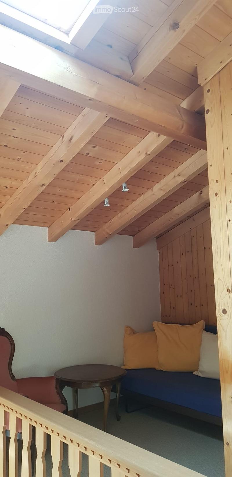 A cozy, wooden-framed loft area with a built-in sofa, small round table, and decorative pillows. The space features exposed wooden beams and a skylight, creating a warm and inviting atmosphere.