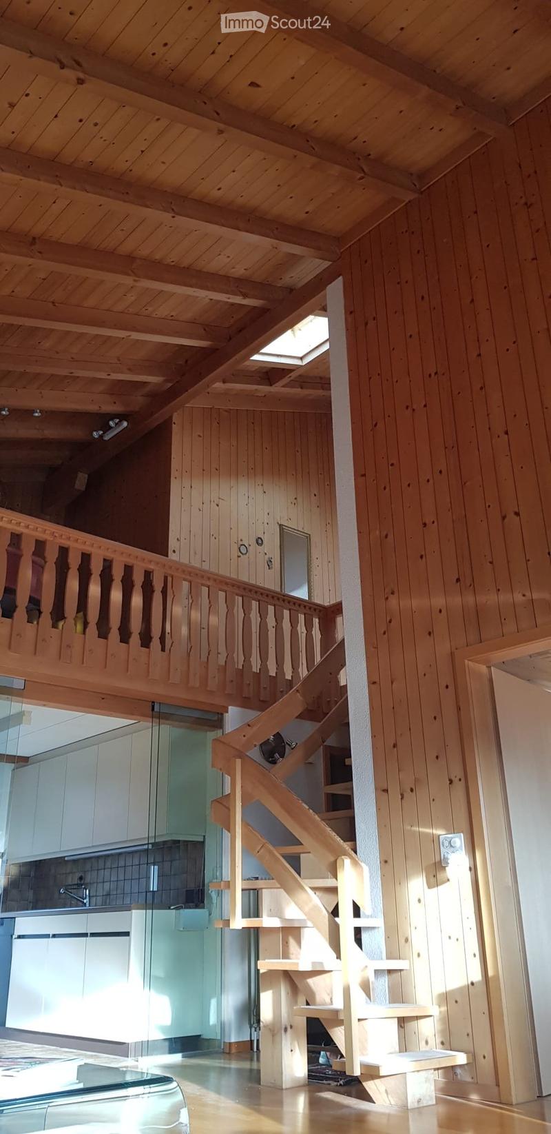 Spacious wooden hallway with a curved staircase leading to an upper level, featuring wooden railings, exposed wooden beams, and large windows allowing natural light to fill the space.