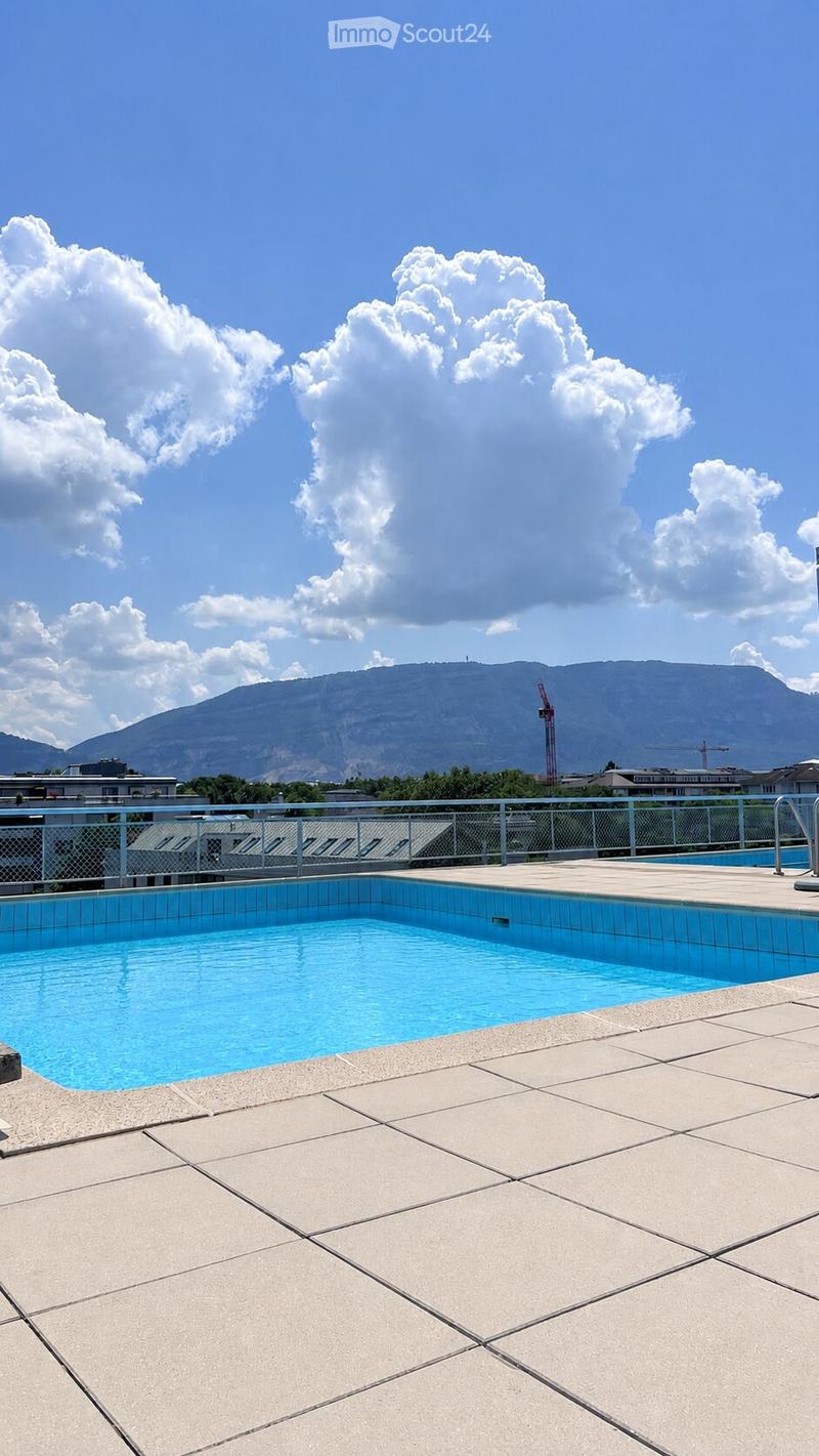 Roof terrace with a swimming pool, tiled deck, metal railing, and a view of mountains and city buildings.