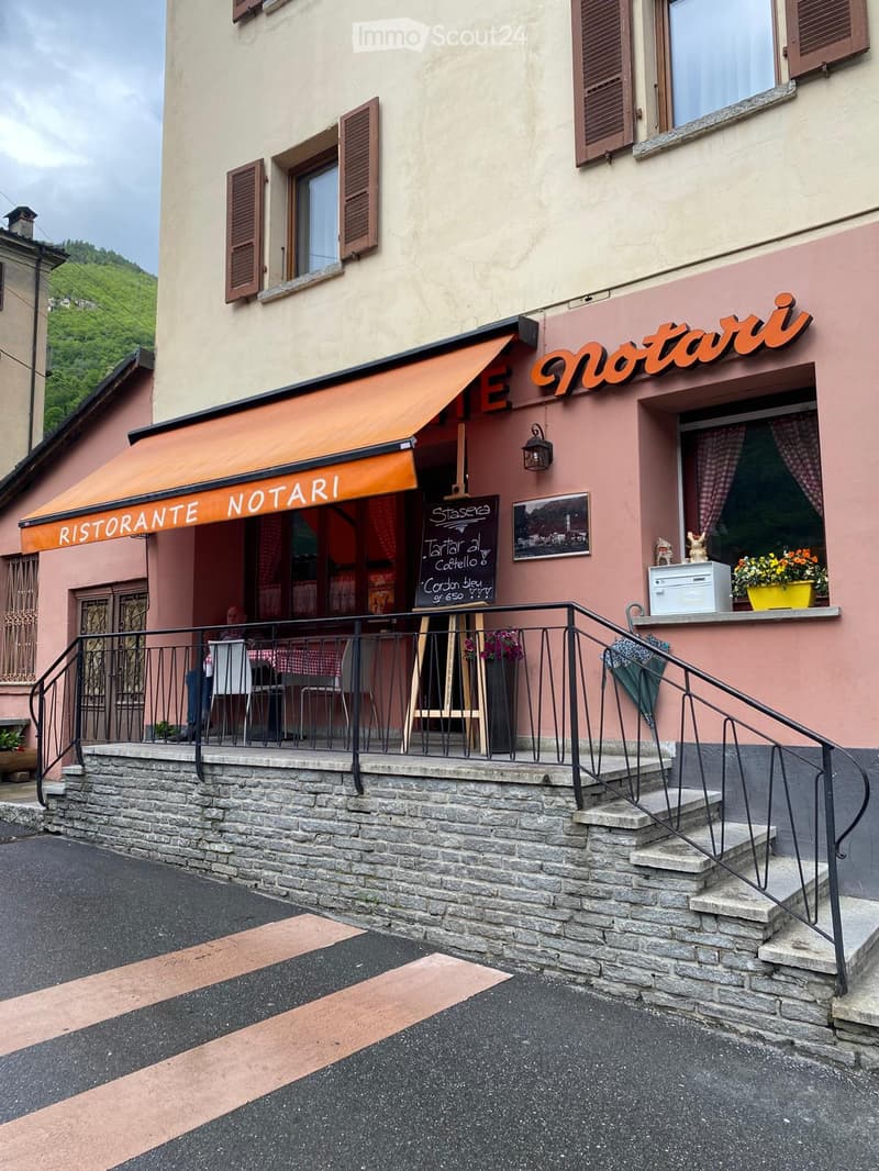 Restaurant facade with an orange awning, stone steps, and outdoor seating area with tables and chairs.