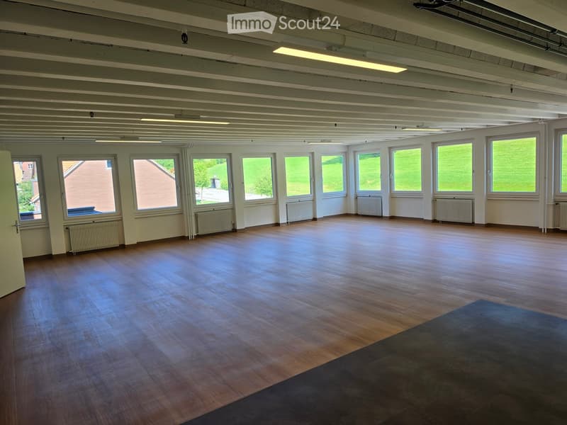 Empty room with wooden flooring, large windows, radiators, and exposed ceiling beams.
