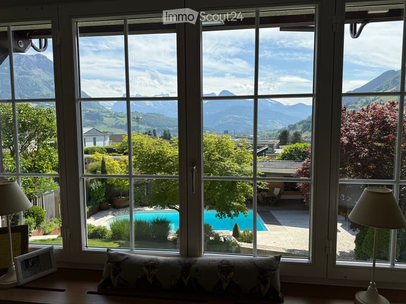 Bright room with large windows offering a scenic mountain view and a swimming pool in the garden.