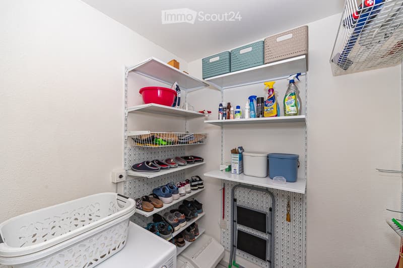Well-organized closet with multiple shelves holding cleaning supplies, shoes, and storage bins. A laundry basket is placed on the floor.