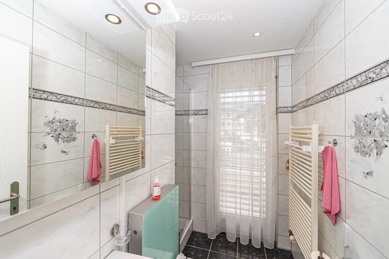 Modern bathroom with white marble tiles, a glass shower enclosure, a radiator, and a towel hanging on the wall.