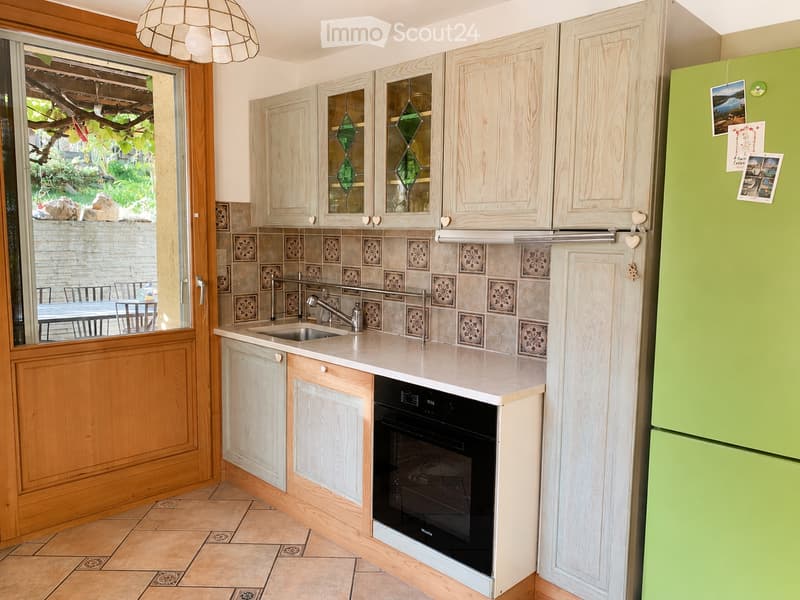 Bright kitchen with light wooden cabinets, a white countertop, a sink, and a green refrigerator. The backsplash features decorative tiles, and a window offers a view of the outdoor area.