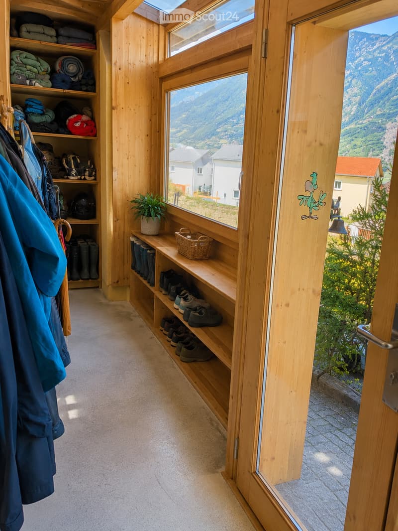 Wooden hallway with built-in shoe rack, coat rack, and storage shelves, leading to a scenic mountain view through large windows.