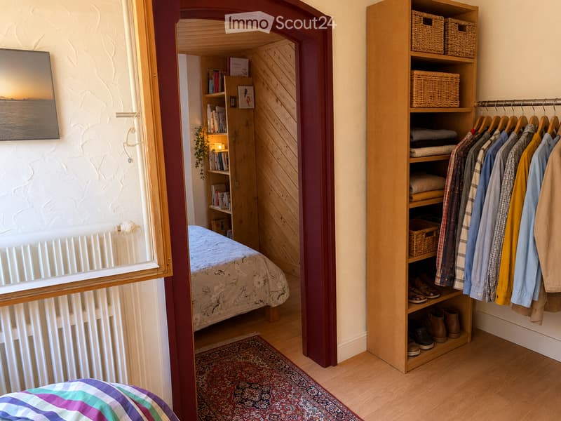 Cozy bedroom with a bed, bookshelf, wardrobe, and a picture frame on the wall. Wooden flooring and a patterned rug are visible.