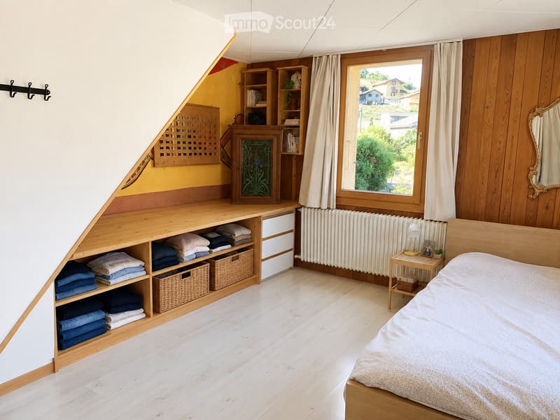 Cozy attic bedroom with wooden walls and floor, large window with view, bed, nightstand, shelves, storage unit, and wicker baskets.