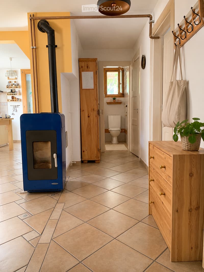 Hallway with tiled floor, wooden cabinet, coat rack, and visible bathroom with toilet and sink.