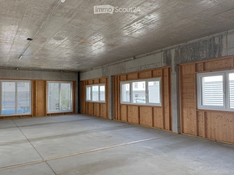 Empty room with concrete floors and walls, wooden paneling, and multiple windows with blinds.