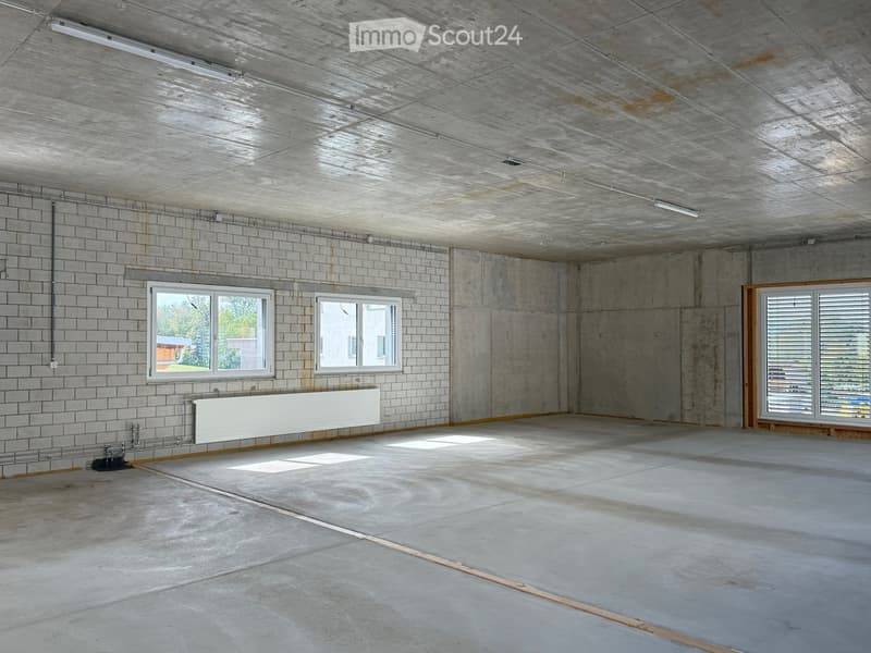 Empty room with concrete walls, tiled section, and windows allowing natural light. No furniture or equipment present.