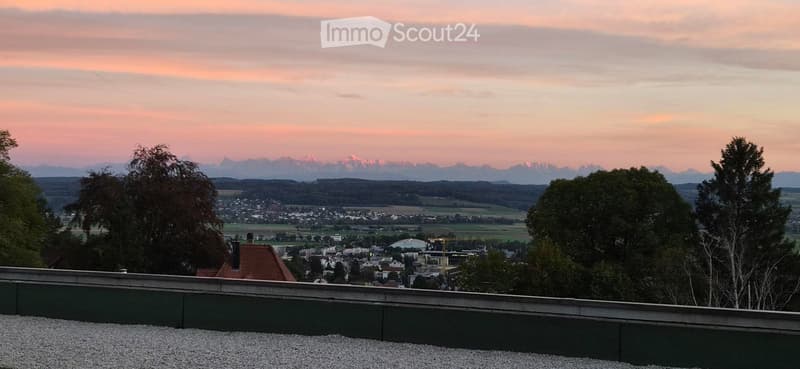 A rooftop terrace with a gravel surface, overlooking a town and distant mountains during sunset.
