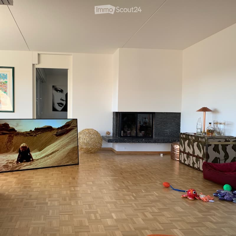 Modern living room with wooden floor, fireplace, large screen, table with lamp, and various toys on the floor.