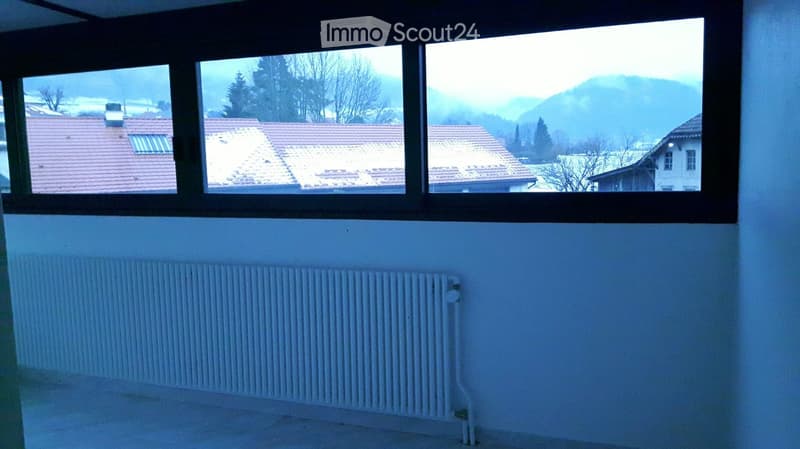 Empty room with white walls, a radiator, and a large window offering a view of a snowy landscape and houses.