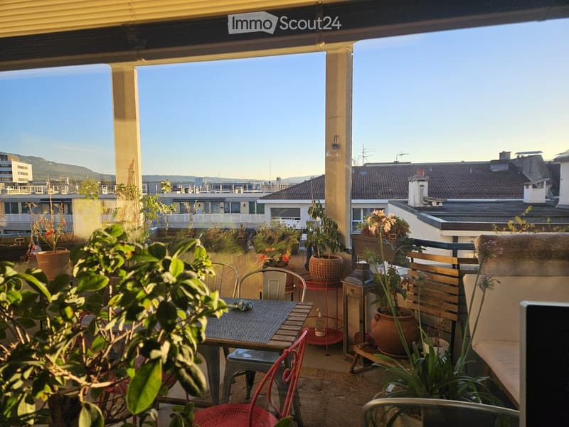 Balcony with outdoor furniture, potted plants, and a view of the city and mountains.