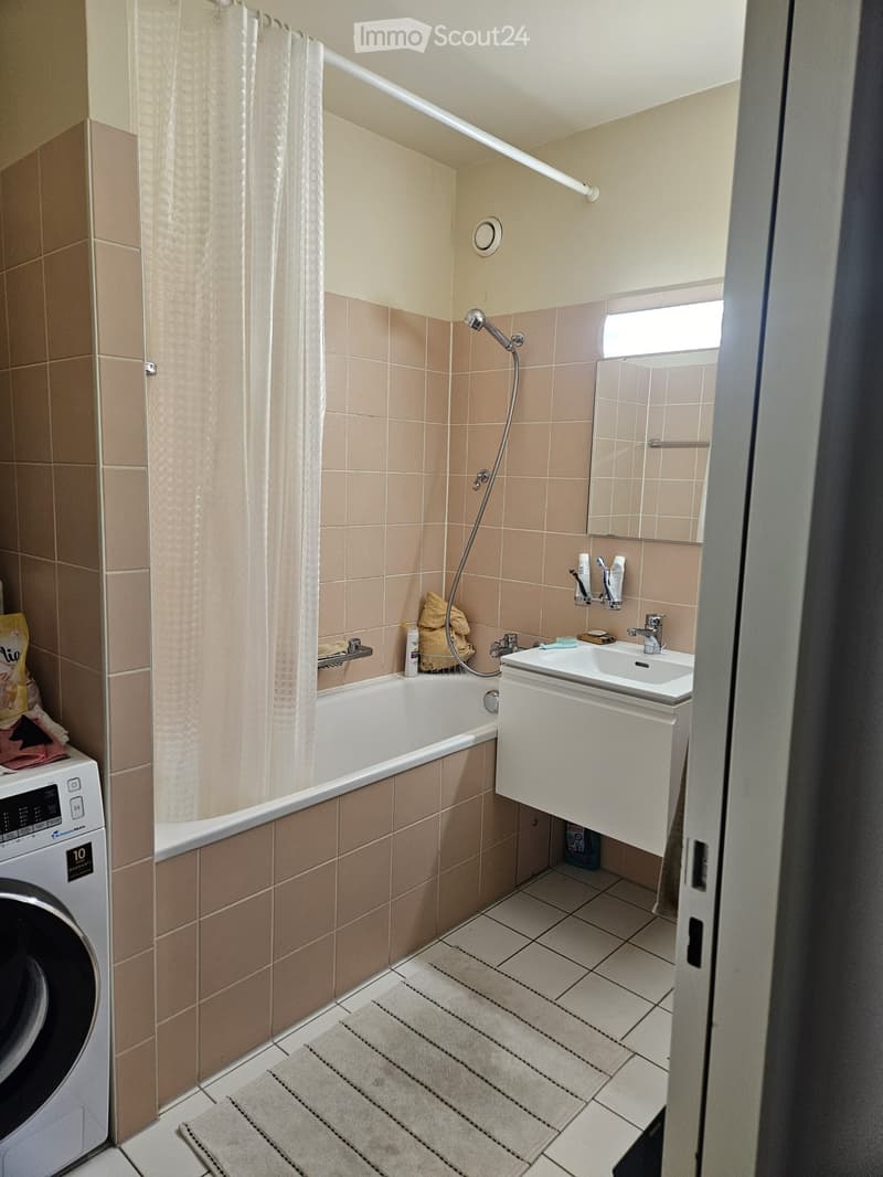 Bathroom with a bathtub, sink, mirror, shower curtain, and a washing machine in the corner.