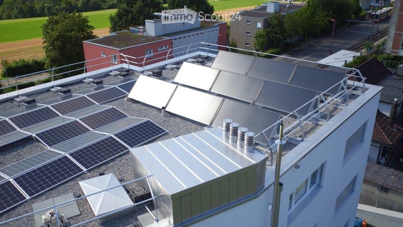 Roof of a building with multiple solar panels, ventilation units, and a small fenced area.
