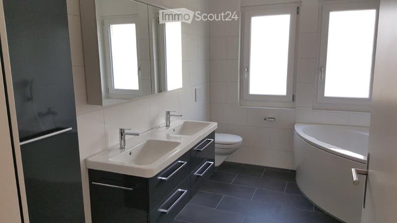 Modern bathroom with double sink vanity, large mirror, toilet, bathtub, and tiled walls and floor.